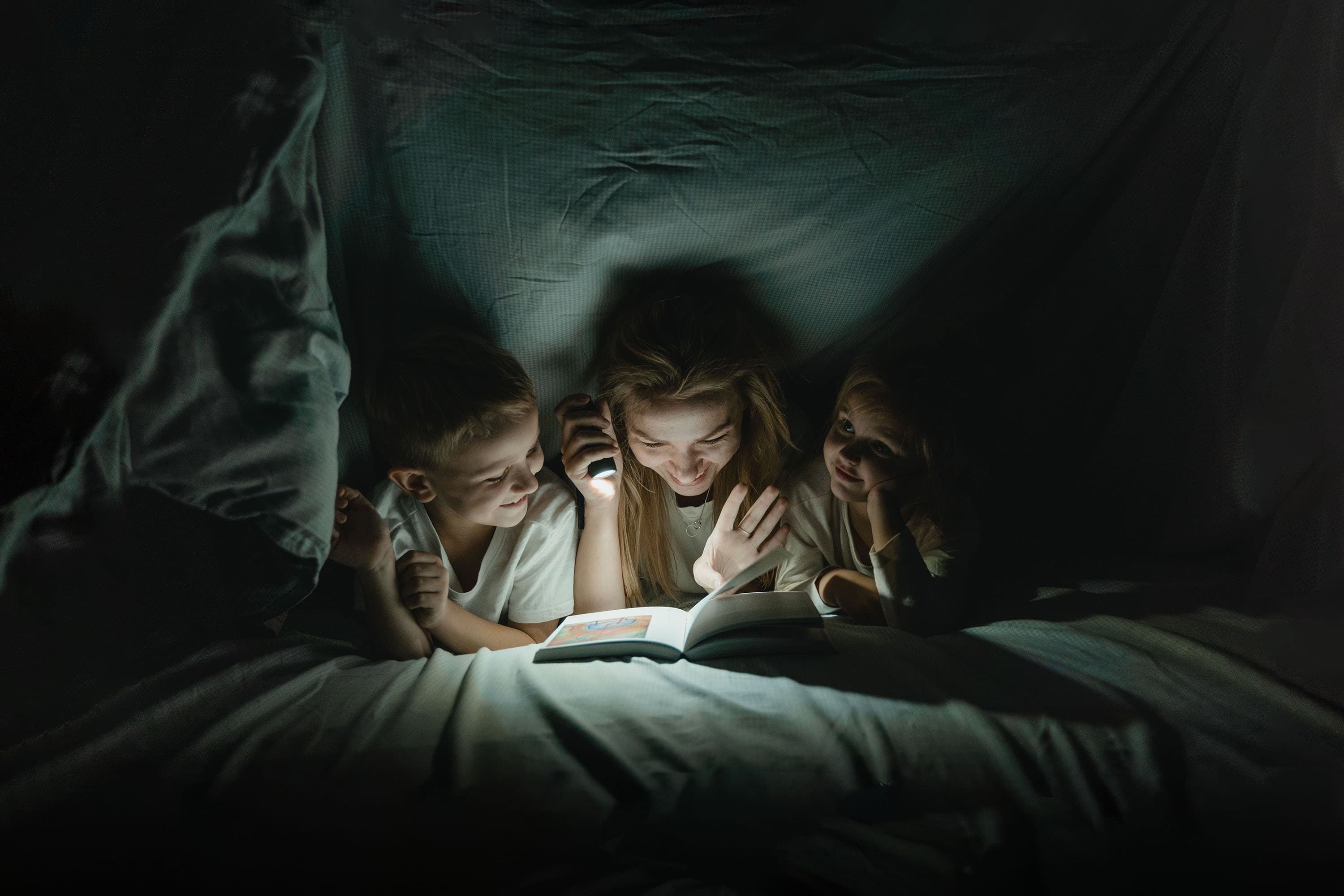 Children reading under the covers with a flashlight.